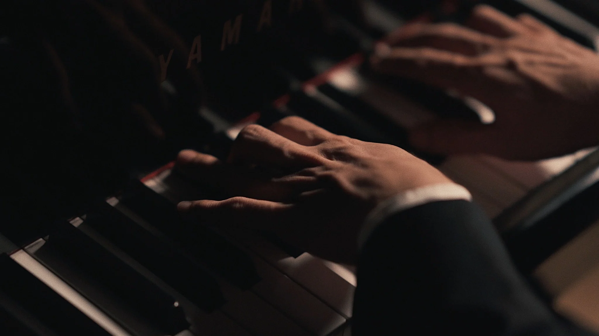 Hands playing a grand piano in warm, dramatic light
