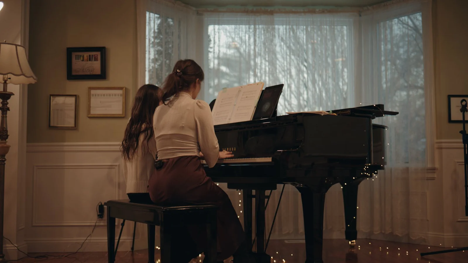 A teacher and student playing side by side at a Yamaha grand