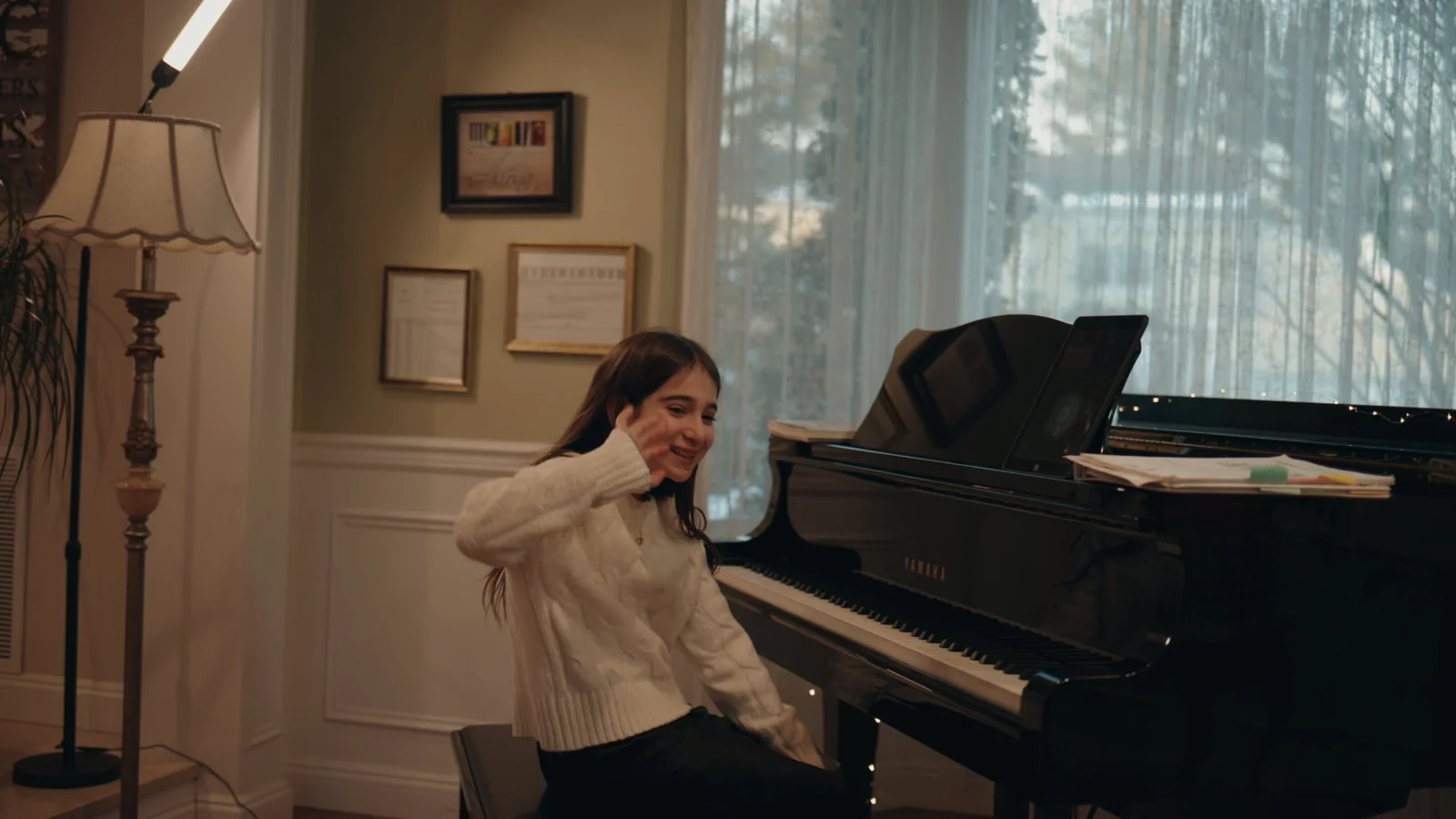 A young student smiling and waving from the bench of a Yamaha grand